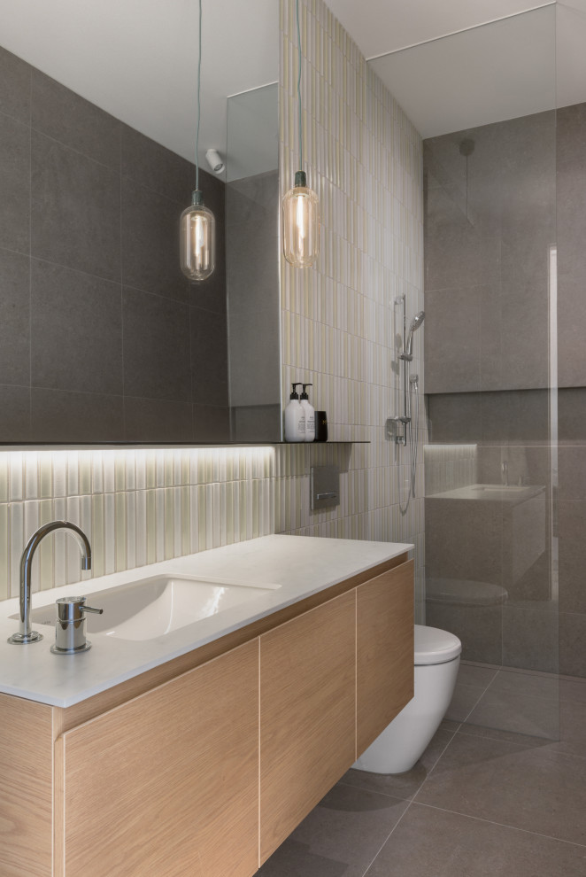 Modernes Badezimmer mit flächenbündigen Schrankfronten, hellen Holzschränken, bodengleicher Dusche, farbigen Fliesen, Unterbauwaschbecken, grauem Boden, offener Dusche, weißer Waschtischplatte, Einzelwaschbecken und schwebendem Waschtisch in Melbourne