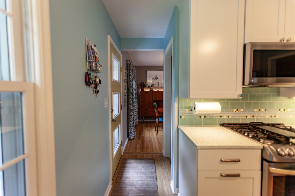 This is an example of a midcentury separate kitchen in Minneapolis with an undermount sink, shaker cabinets, white cabinets, recycled glass benchtops, green splashback, mosaic tile splashback, stainless steel appliances, medium hardwood floors, no island, brown floor and white benchtop.