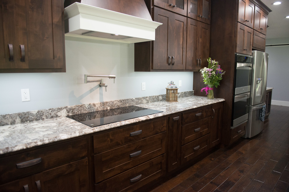 Example of a transitional l-shaped open concept kitchen design with an undermount sink, shaker cabinets, dark wood cabinets, granite countertops, stainless steel appliances, an island and multicolored countertops