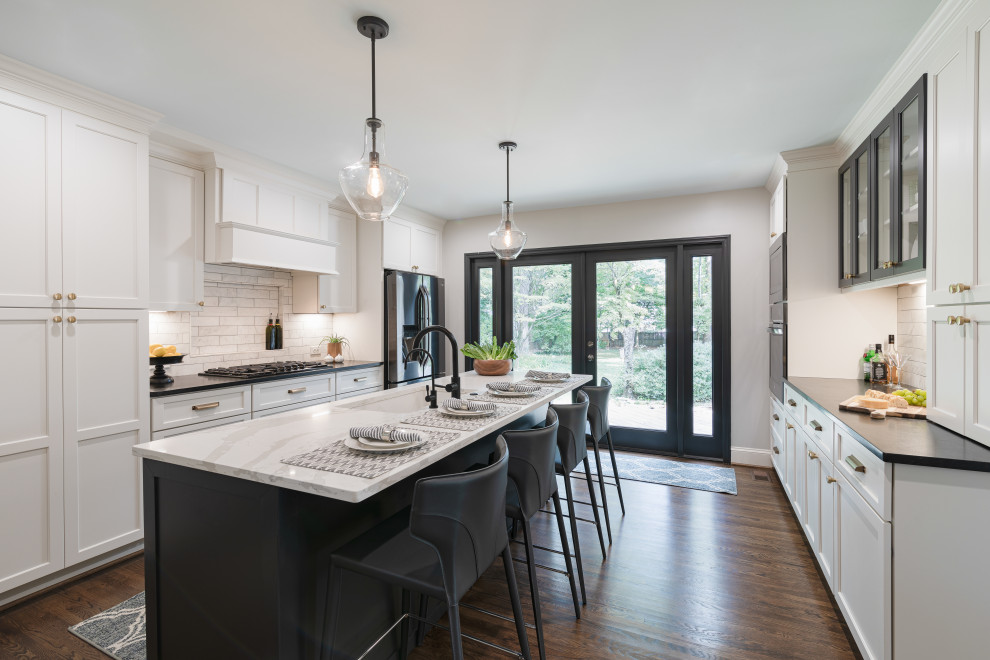 Photo of a mid-sized modern galley kitchen in Other with a single-bowl sink, shaker cabinets, white cabinets, quartz benchtops, grey splashback, marble splashback, stainless steel appliances, medium hardwood floors, with island, brown floor and black benchtop.