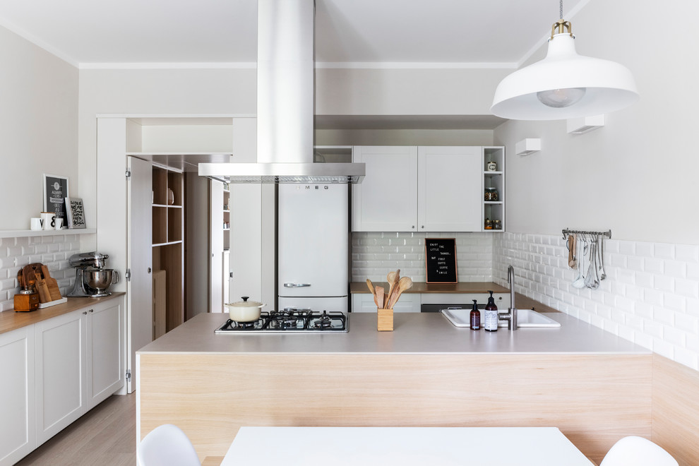 Design ideas for a mid-sized scandinavian single-wall eat-in kitchen in Milan with a drop-in sink, recessed-panel cabinets, white cabinets, wood benchtops, white splashback, subway tile splashback, stainless steel appliances, light hardwood floors, with island and beige benchtop.