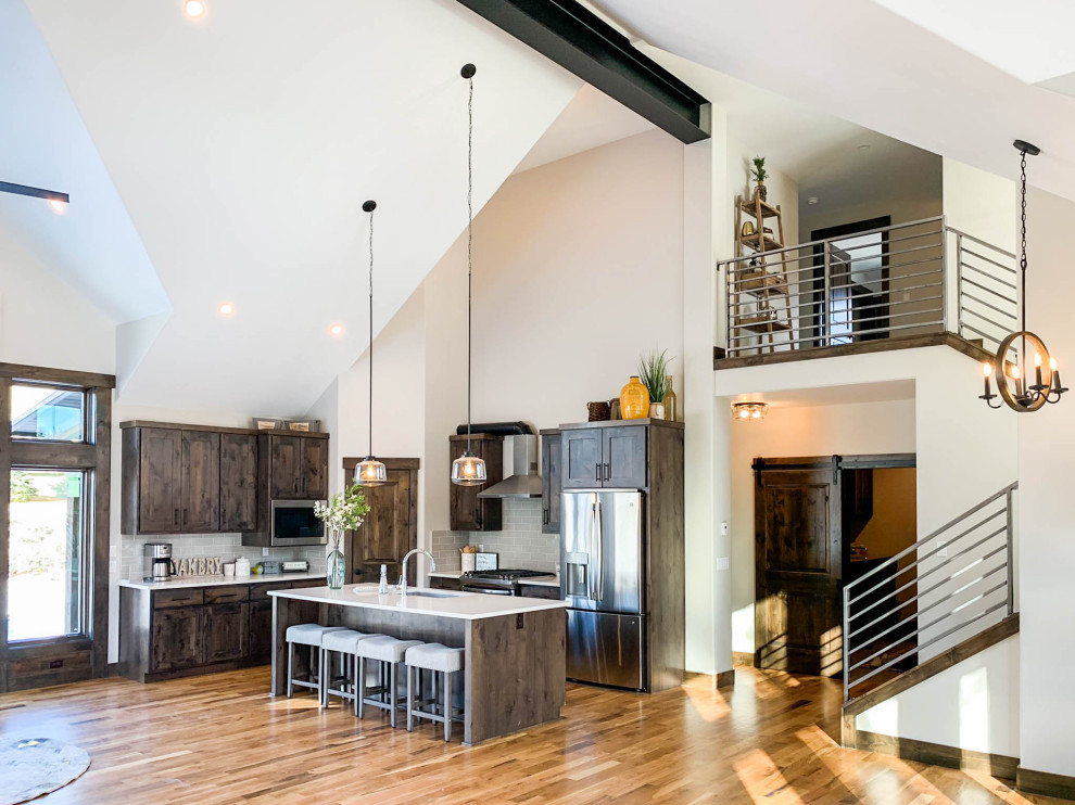 Inspiration for an expansive modern l-shaped open plan kitchen in Denver with a drop-in sink, shaker cabinets, distressed cabinets, quartz benchtops, grey splashback, subway tile splashback, stainless steel appliances, light hardwood floors, with island, brown floor and white benchtop.