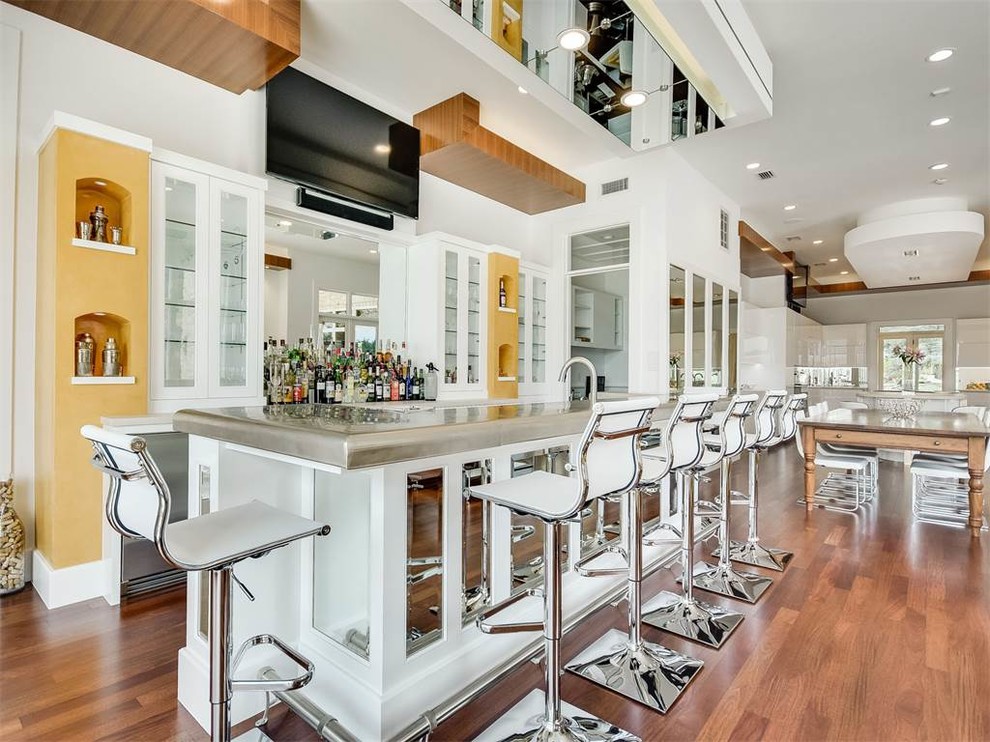 Inspiration for a large contemporary single-wall seated home bar in Austin with a drop-in sink, glass-front cabinets, white cabinets, stainless steel benchtops, white splashback, mirror splashback and medium hardwood floors.