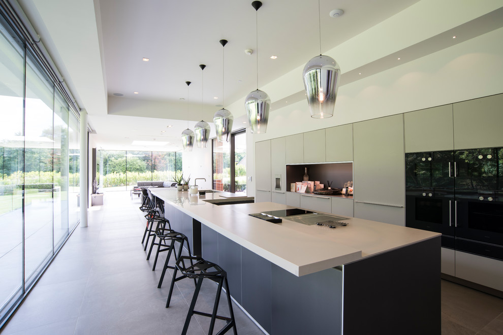 Design ideas for an expansive contemporary single-wall open plan kitchen in London with an integrated sink, flat-panel cabinets, grey cabinets, solid surface benchtops, white splashback, panelled appliances, porcelain floors, a peninsula and grey floor.