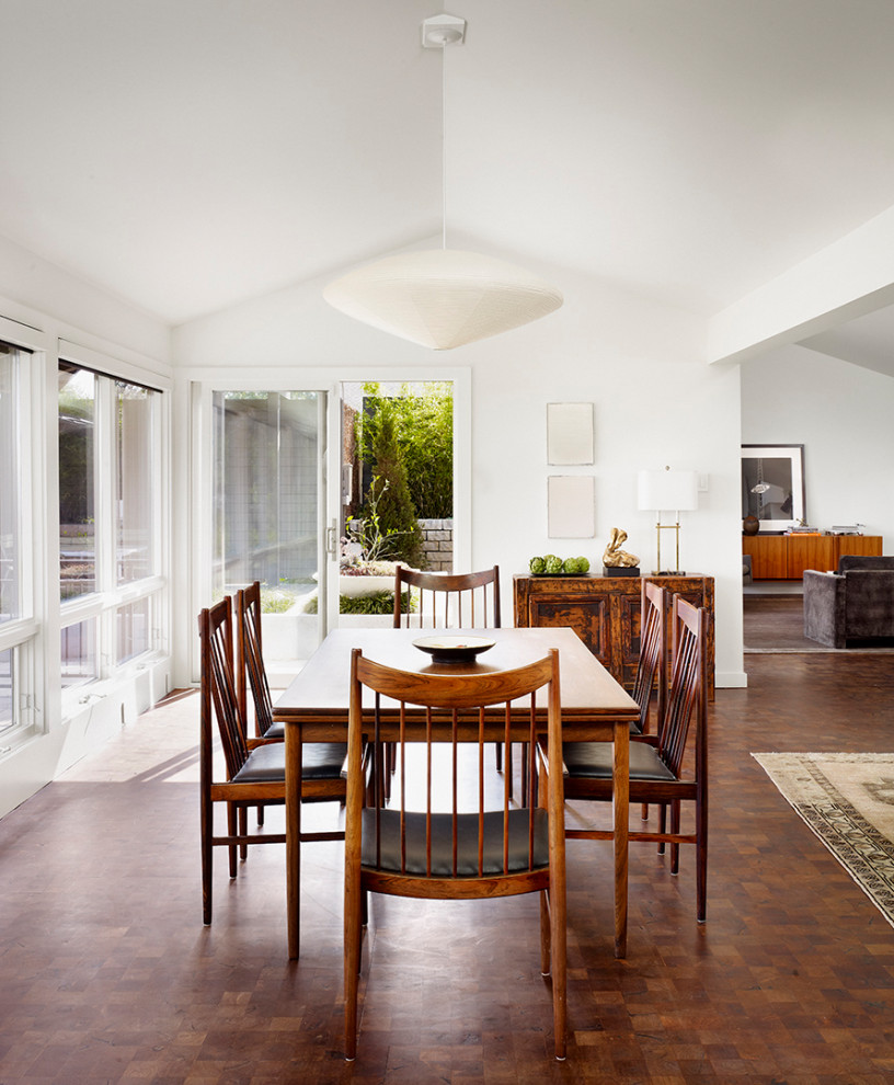 This is an example of a midcentury open plan dining in Austin with white walls, brown floor, no fireplace and vaulted.