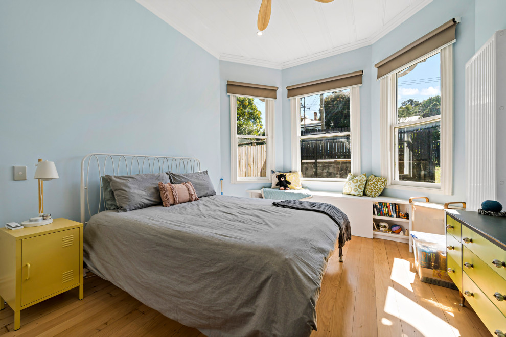Bild på ett stort könsneutralt tonårsrum kombinerat med sovrum, med blå väggar, mellanmörkt trägolv och brunt golv
