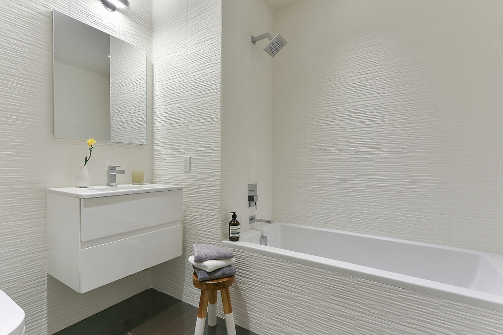 This is an example of a contemporary bathroom in New York with flat-panel cabinets, white cabinets, a drop-in tub, a shower/bathtub combo and white tile.