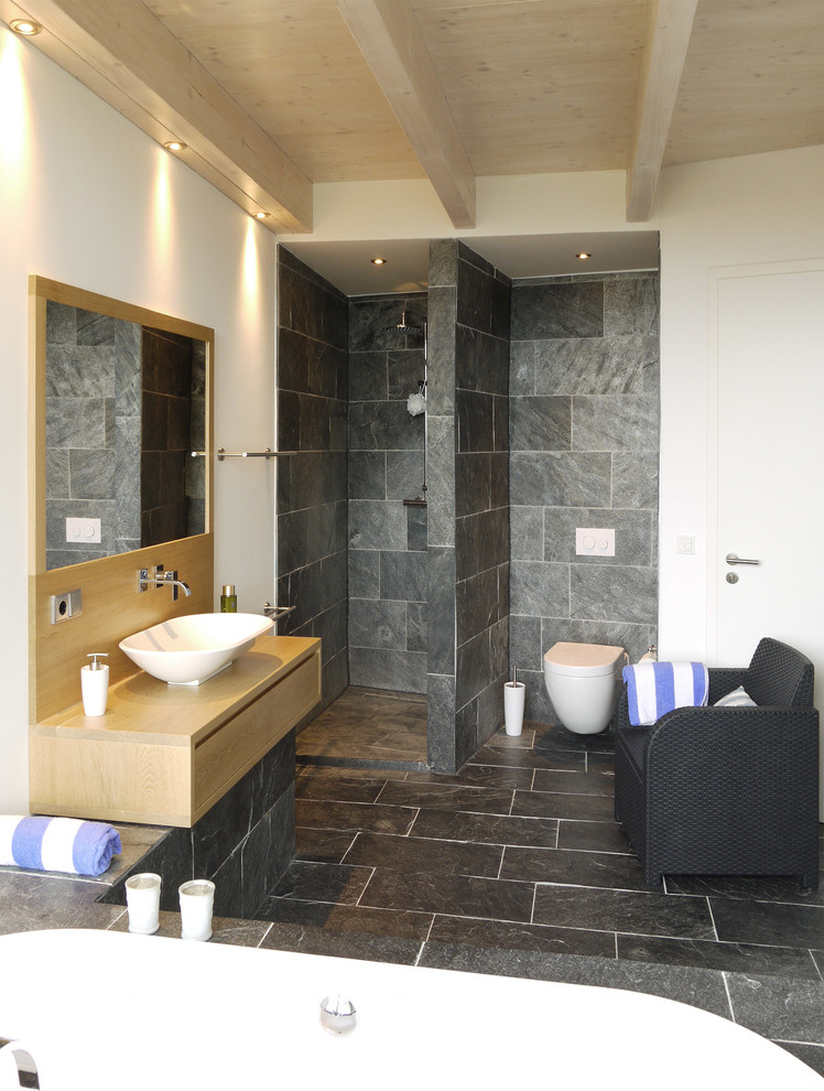 Badezimmer With hellen Holzschränken, Einbaubadewanne, schwarzen Fliesen, Steinplatten, weißer Wandfarbe, Schieferboden, Aufsatzwaschbecken, flächenbündigen Schrankfronten, Wandtoilette, Waschtisch aus Holz and offener Dusche in Hanover