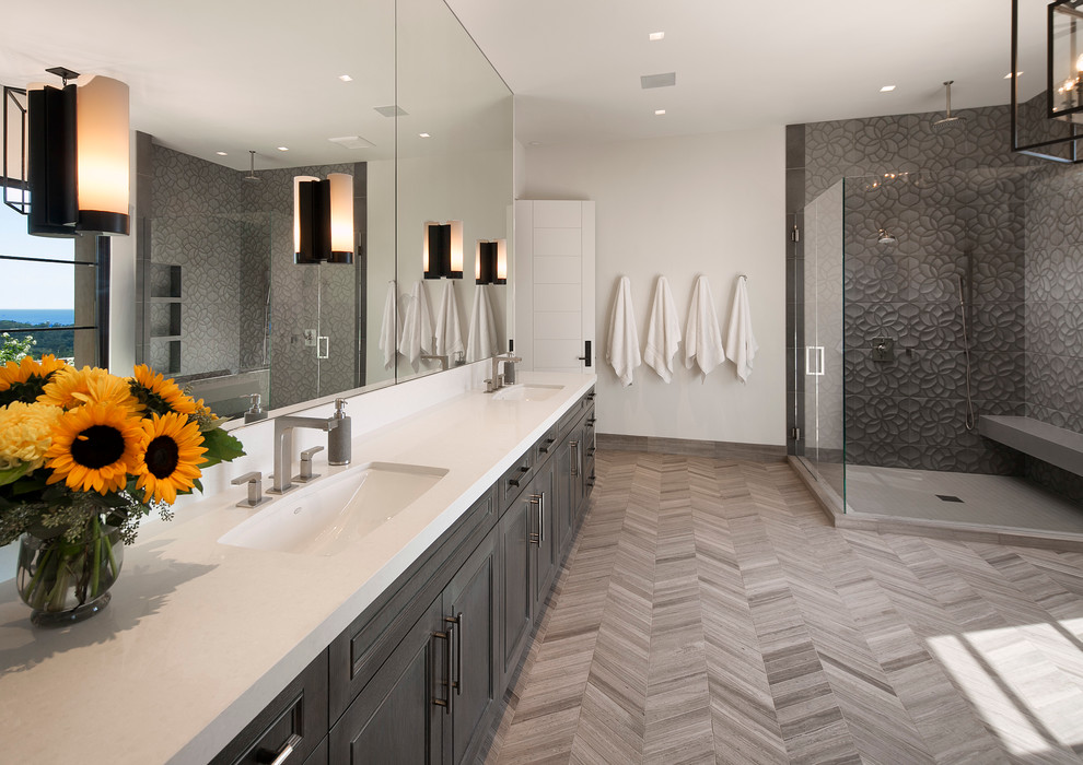 Design ideas for a large contemporary master bathroom in Santa Barbara with an undermount sink, recessed-panel cabinets, grey cabinets, a corner shower, gray tile, white walls, light hardwood floors, solid surface benchtops and a shower seat.