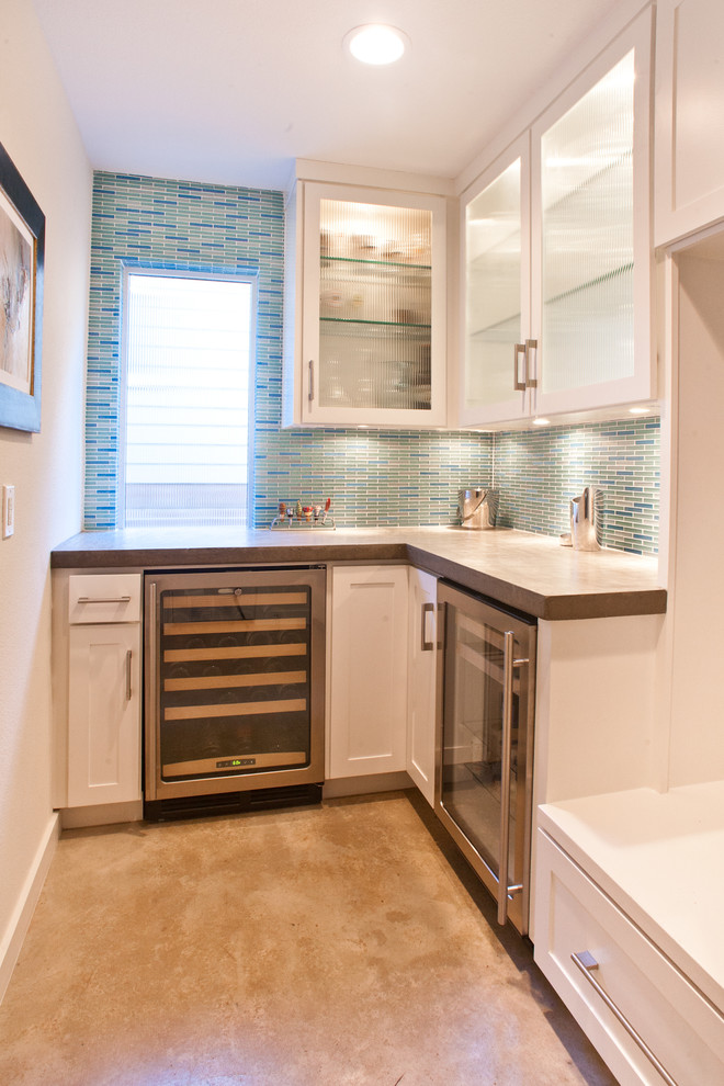 Mid-sized transitional l-shaped wet bar in Dallas with no sink, glass-front cabinets, white cabinets, solid surface benchtops, blue splashback, matchstick tile splashback, concrete floors and grey floor.