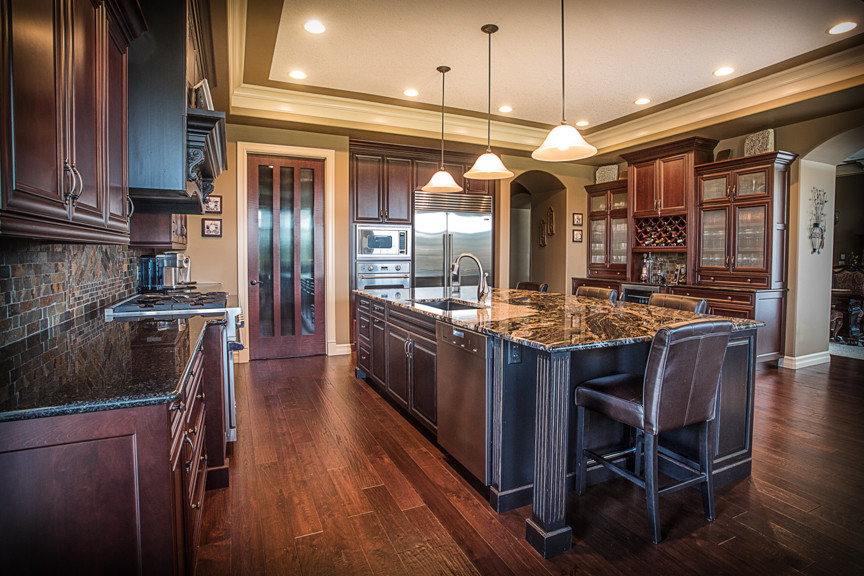 This is an example of a large traditional u-shaped kitchen in Edmonton with an undermount sink, recessed-panel cabinets, dark wood cabinets, granite benchtops, multi-coloured splashback, slate splashback, stainless steel appliances, dark hardwood floors, with island, brown floor and multi-coloured benchtop.