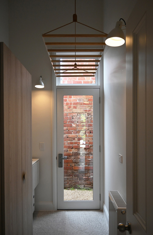 Mid-sized contemporary galley dedicated laundry room with an integrated sink, open cabinets, light wood cabinets, white splashback, mosaic tile splashback, white walls, ceramic floors, a stacked washer and dryer, multi-coloured floor and white benchtop.