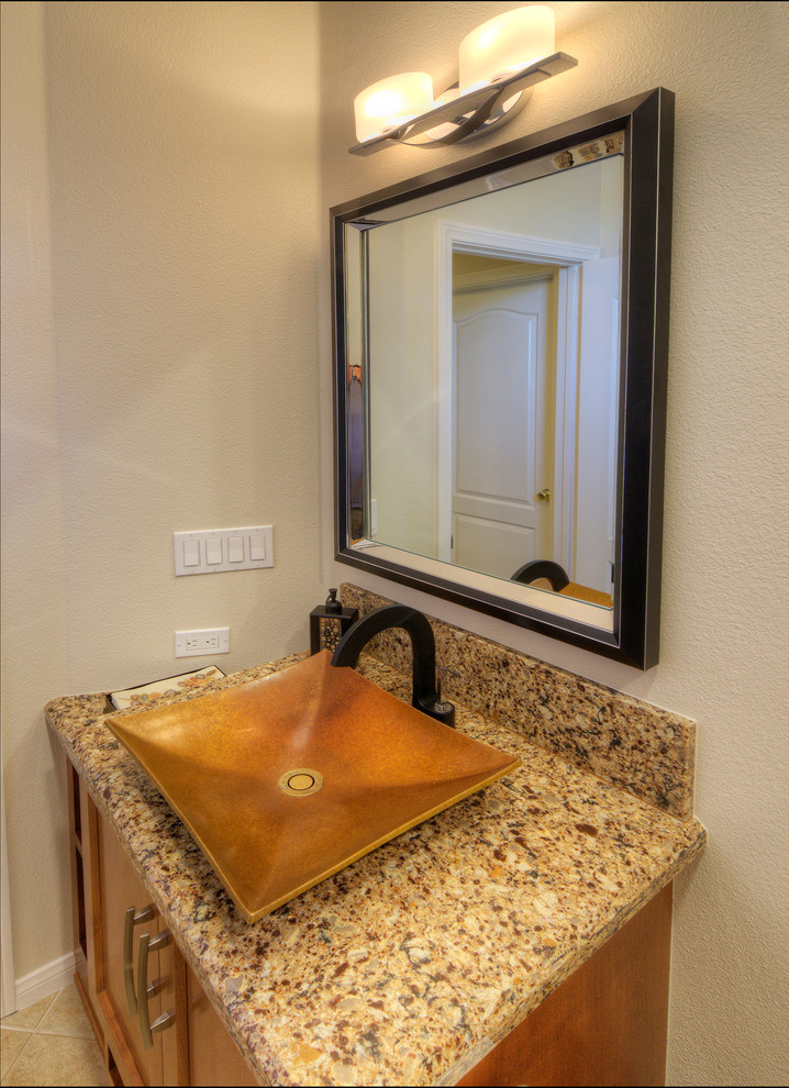 Design ideas for a mid-sized contemporary powder room in San Diego with recessed-panel cabinets, brown cabinets, a two-piece toilet, beige tile, ceramic tile, beige walls, travertine floors, a vessel sink, granite benchtops, brown floor and brown benchtops.
