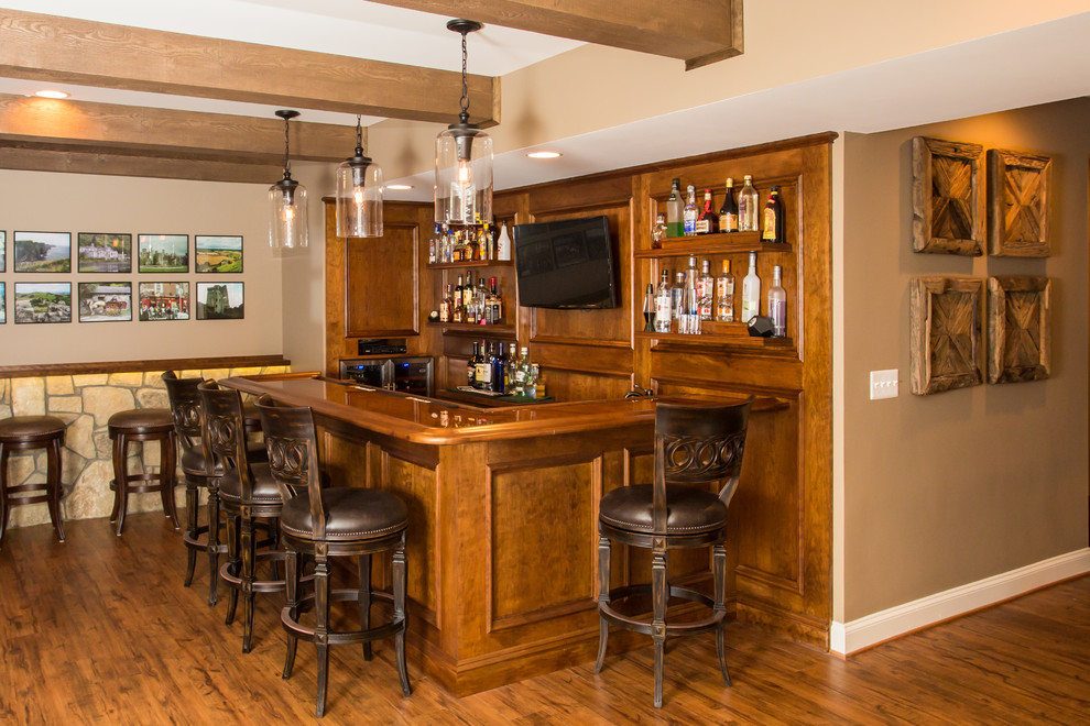 This is an example of a mid-sized country l-shaped seated home bar in DC Metro with an undermount sink, dark wood cabinets, wood benchtops, brown splashback, timber splashback, brown floor and medium hardwood floors.