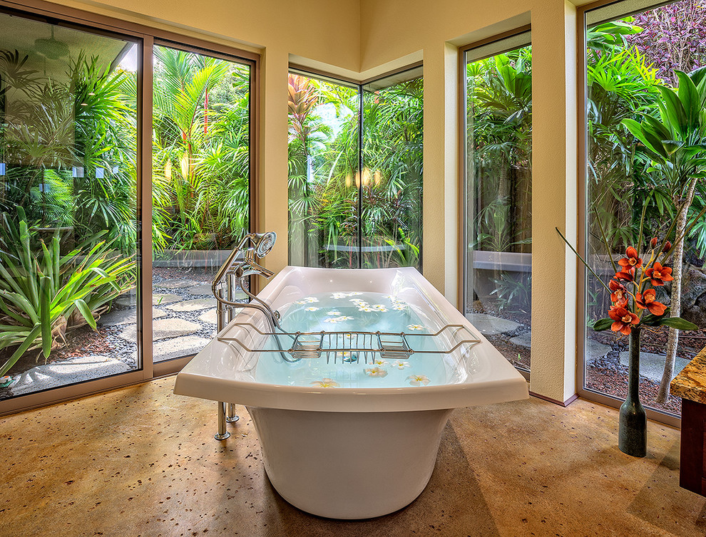 Inspiration for an expansive tropical master bathroom in Hawaii with a drop-in sink, recessed-panel cabinets, medium wood cabinets, granite benchtops, a freestanding tub, a double shower, beige tile, stone slab, beige walls and concrete floors.