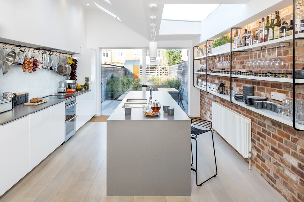 Inspiration for a mid-sized contemporary kitchen in London with flat-panel cabinets, white cabinets, light hardwood floors, with island, a double-bowl sink, concrete benchtops, stainless steel appliances, grey benchtop, white splashback, glass sheet splashback and beige floor.