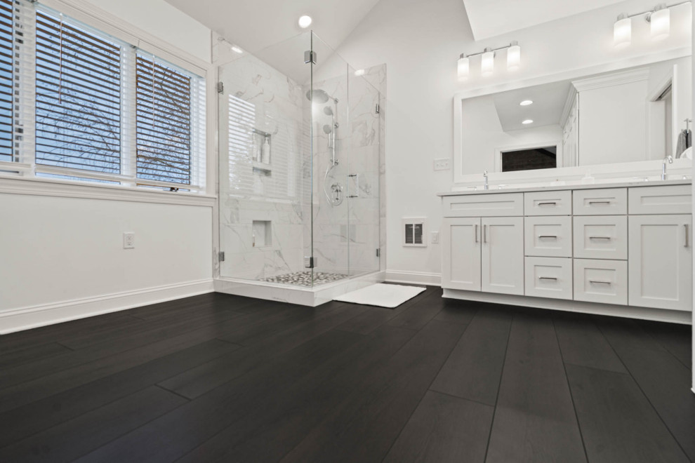Photo of a mid-sized modern master bathroom in DC Metro with beaded inset cabinets, white cabinets, a corner shower, a one-piece toilet, white tile, marble, white walls, vinyl floors, a drop-in sink, marble benchtops, brown floor, a hinged shower door, white benchtops, a double vanity, a built-in vanity and vaulted.