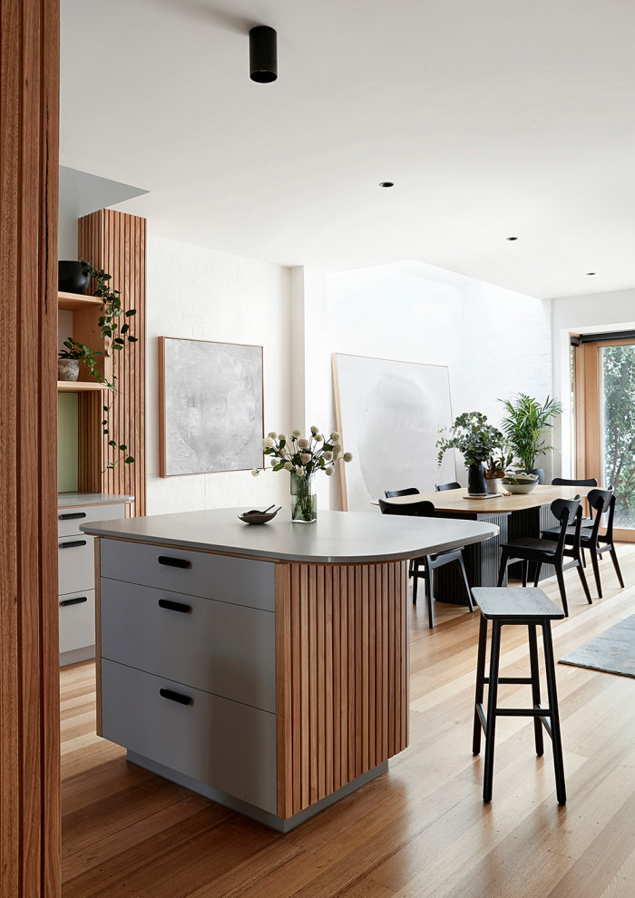 Photo of a medium sized contemporary u-shaped open plan kitchen in Melbourne with a submerged sink, flat-panel cabinets, grey cabinets, engineered stone countertops, grey splashback, glass sheet splashback, black appliances, light hardwood flooring, an island, brown floors and grey worktops.