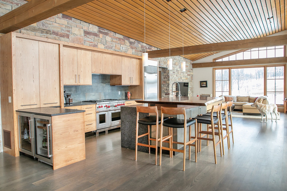 Open concept kitchen - large rustic l-shaped medium tone wood floor and brown floor open concept kitchen idea with flat-panel cabinets, light wood cabinets, granite countertops, black backsplash, stainless steel appliances, an island, black countertops, a double-bowl sink and porcelain backsplash