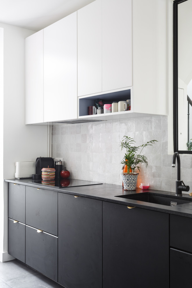 Photo of a scandinavian kitchen in Paris with a single-bowl sink, flat-panel cabinets, grey splashback, grey floor and black benchtop.