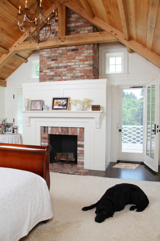 This is an example of a large country master bedroom in Boston with white walls, carpet, a standard fireplace, a brick fireplace surround and beige floor.