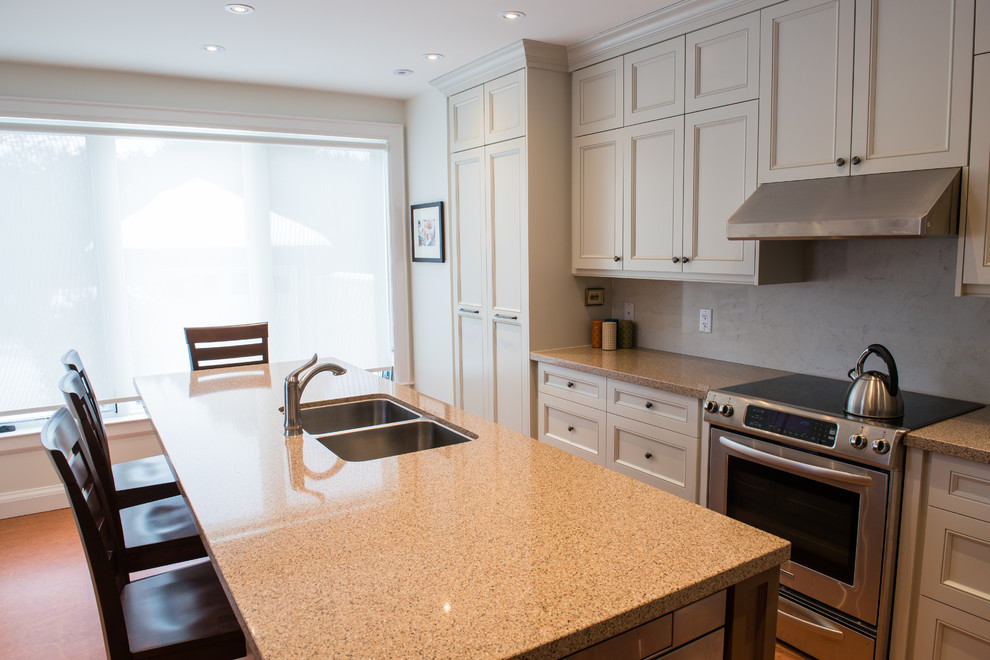 Large traditional l-shaped eat-in kitchen in Toronto with a double-bowl sink, recessed-panel cabinets, beige cabinets, limestone benchtops, white splashback, stone slab splashback, stainless steel appliances, cork floors and with island.