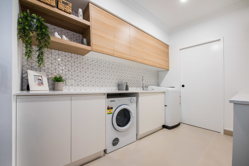 Design ideas for a mid-sized contemporary galley dedicated laundry room in Other with an undermount sink, flat-panel cabinets, light wood cabinets, granite benchtops, white splashback, ceramic splashback, white walls, ceramic floors, a side-by-side washer and dryer, white floor and white benchtop.