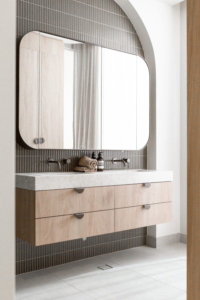 Foto på ett funkis grå badrum, med släta luckor, skåp i ljust trä, grå kakel, vita väggar, ett integrerad handfat, grått golv och stickkakel