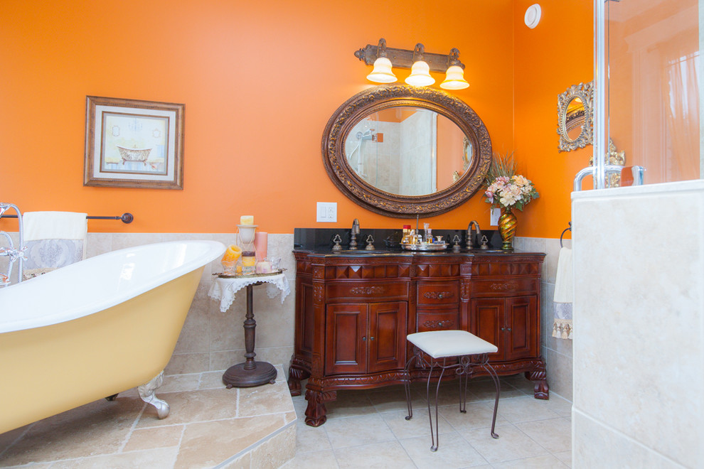 Inspiration for a traditional bathroom in Toronto with dark wood cabinets, a claw-foot tub, beige tile, stone tile and orange walls.