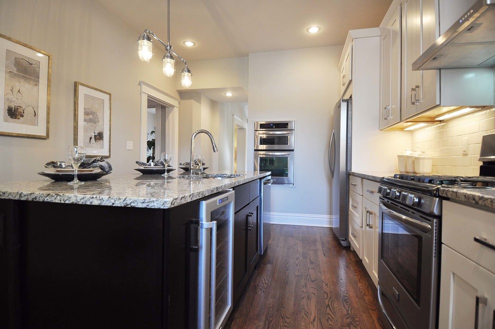 Enclosed kitchen - mid-sized transitional galley medium tone wood floor enclosed kitchen idea in St Louis with an undermount sink, shaker cabinets, granite countertops, white backsplash, subway tile backsplash, stainless steel appliances, an island and white cabinets