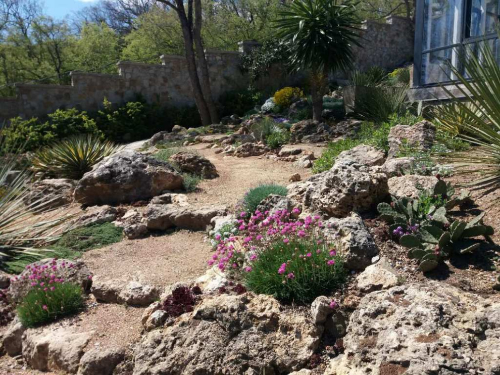 Aménagement d'un grand xéropaysage méditerranéen l'été avec pierres et graviers, une exposition ensoleillée, une pente, une colline ou un talus et une clôture en pierre.