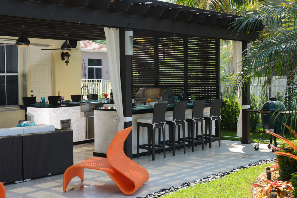 This is an example of an expansive contemporary backyard patio in Miami with an outdoor kitchen, natural stone pavers and a pergola.