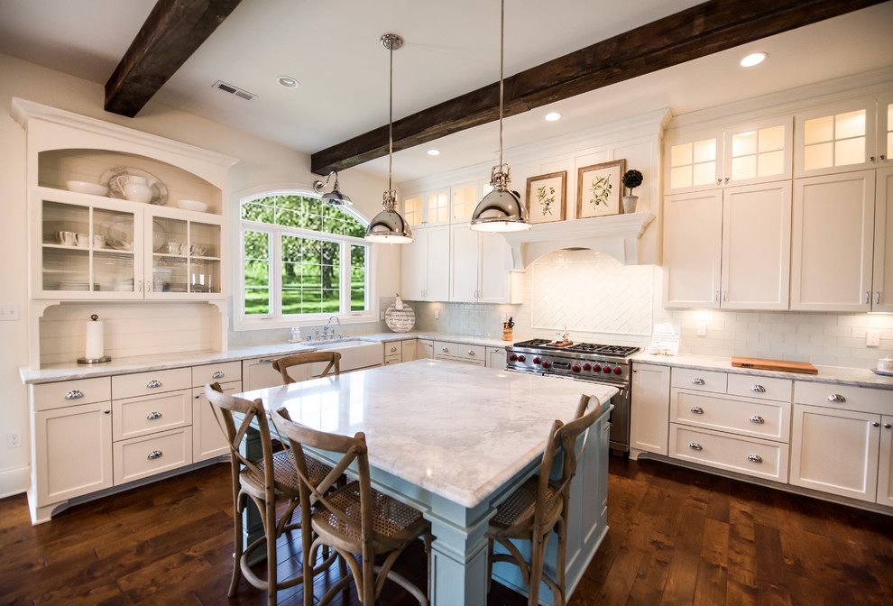 Photo of a traditional l-shaped kitchen in Louisville with a farmhouse sink, shaker cabinets, white cabinets, white splashback, subway tile splashback, stainless steel appliances, dark hardwood floors, with island and brown floor.