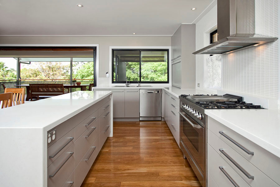 Photo of a mid-sized contemporary l-shaped open plan kitchen in Brisbane with a double-bowl sink, flat-panel cabinets, grey cabinets, white splashback, matchstick tile splashback, stainless steel appliances, medium hardwood floors, with island and brown floor.