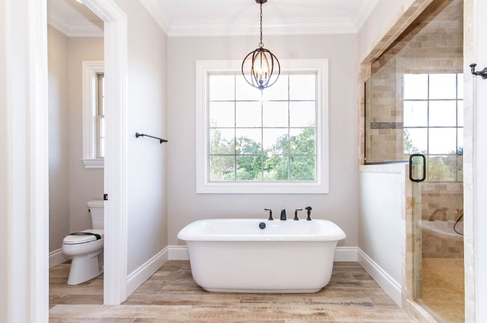 Example of a large transitional master beige tile and stone tile vinyl floor and beige floor freestanding bathtub design with a two-piece toilet, beige walls and a hinged shower door