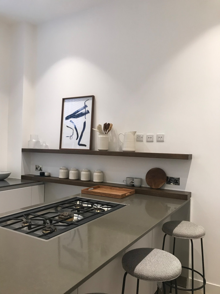 This is an example of a large modern u-shaped separate kitchen in London with an integrated sink, flat-panel cabinets, beige cabinets, solid surface benchtops, black appliances, porcelain floors, with island, beige floor and green benchtop.