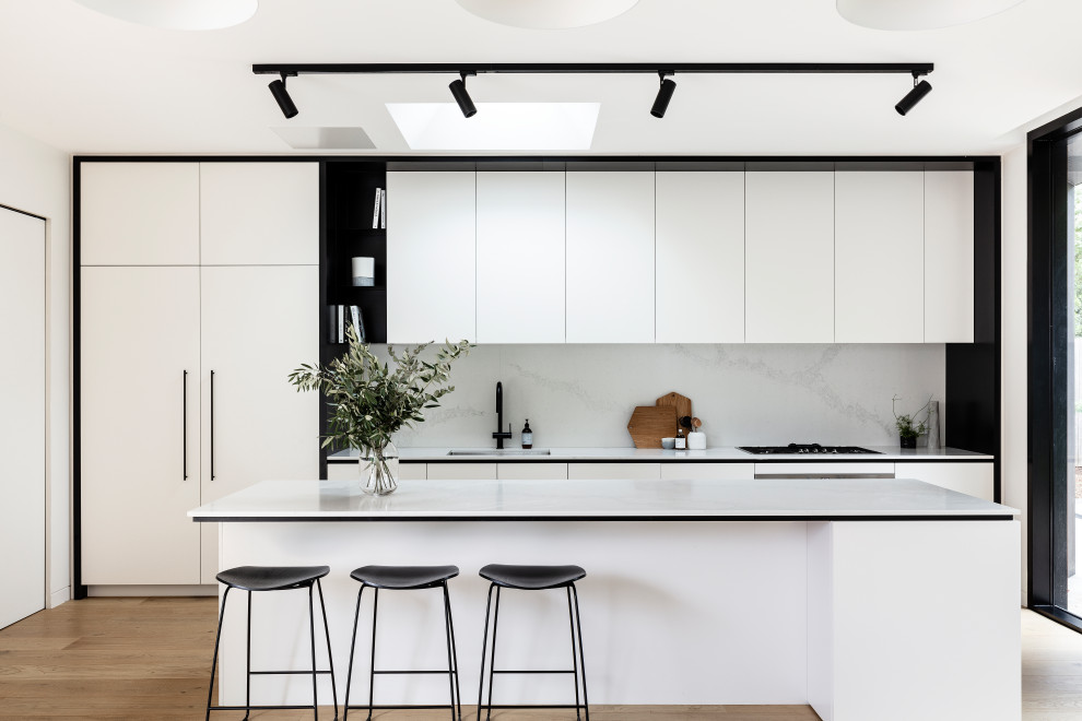 Inspiration for a contemporary galley kitchen in Sydney with an undermount sink, flat-panel cabinets, white cabinets, white splashback, stone slab splashback, medium hardwood floors, with island, brown floor and white benchtop.