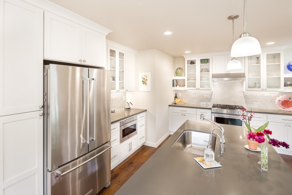 Mid-sized transitional l-shaped medium tone wood floor eat-in kitchen photo with an undermount sink, flat-panel cabinets, white cabinets, quartz countertops, gray backsplash, ceramic backsplash, stainless steel appliances and an island