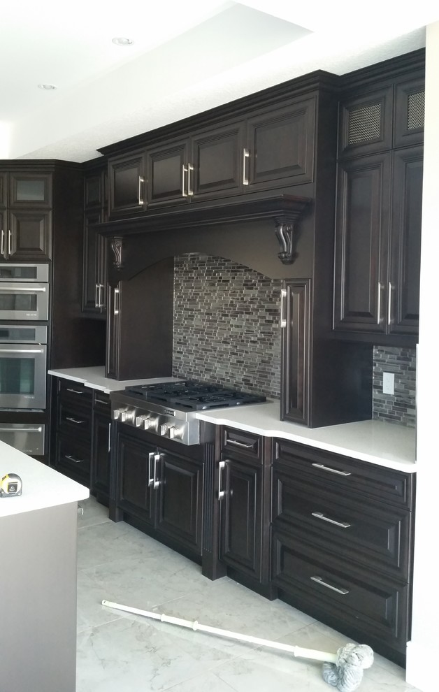 Photo of a large contemporary l-shaped kitchen in Edmonton with raised-panel cabinets, dark wood cabinets, solid surface benchtops, grey splashback, matchstick tile splashback, stainless steel appliances, marble floors and with island.