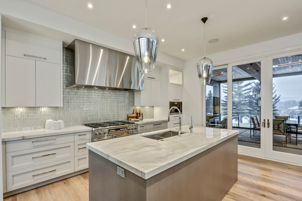 Photo of a large contemporary galley eat-in kitchen in Calgary with flat-panel cabinets, white cabinets, white splashback, stainless steel appliances, light hardwood floors and multiple islands.