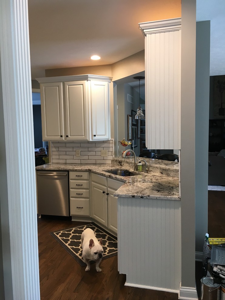Example of a mid-sized transitional u-shaped medium tone wood floor and brown floor kitchen pantry design in Indianapolis with an undermount sink, raised-panel cabinets, white cabinets, granite countertops, white backsplash, ceramic backsplash, stainless steel appliances, no island and white countertops