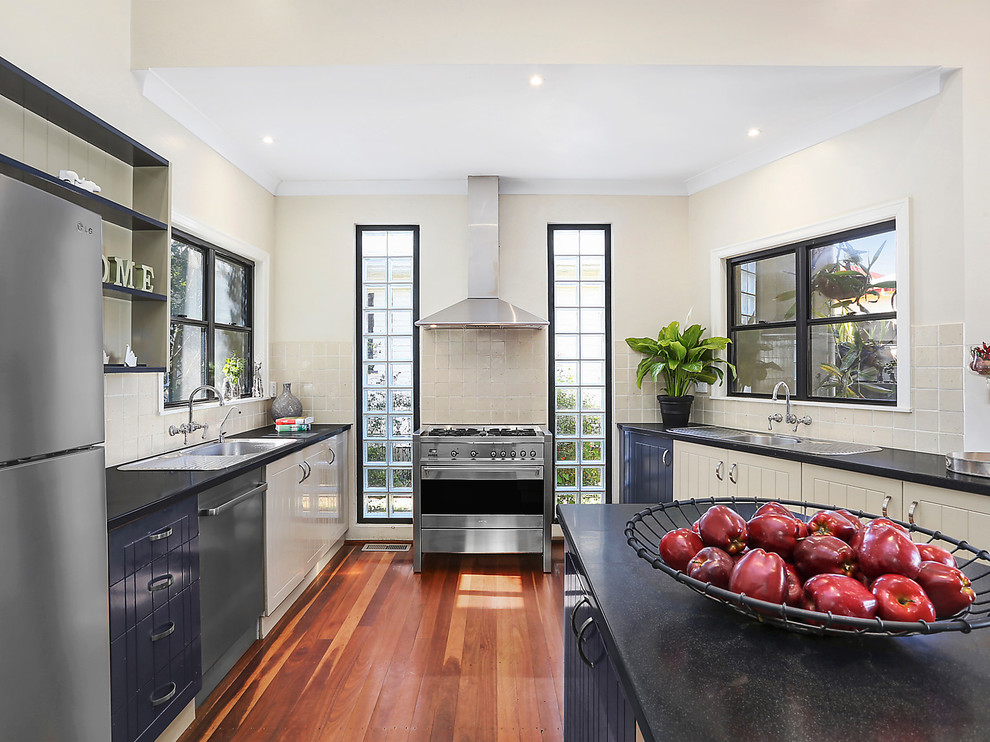 Inspiration for a large transitional open plan kitchen in Brisbane with a single-bowl sink, blue cabinets, laminate benchtops, beige splashback, ceramic splashback, stainless steel appliances, light hardwood floors and with island.