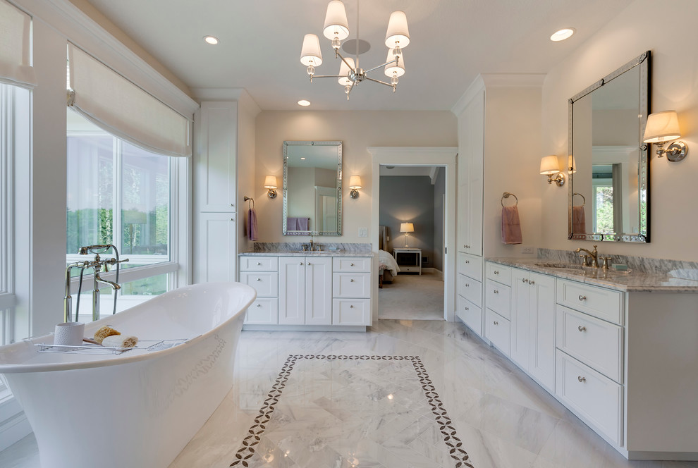 Traditional bathroom in Minneapolis with an undermount sink, recessed-panel cabinets, white cabinets, a freestanding tub, white tile, beige walls, stone tile and porcelain floors.