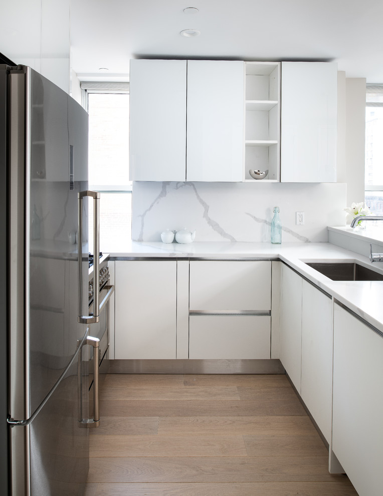 Photo of a mid-sized modern u-shaped kitchen in New York with glass-front cabinets, white cabinets, glass benchtops, white splashback, a peninsula and white benchtop.