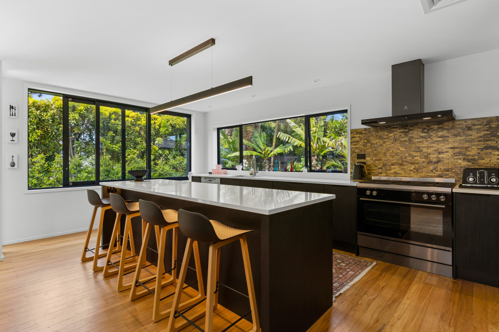 Mid-sized minimalist galley medium tone wood floor and brown floor eat-in kitchen photo with a single-bowl sink, solid surface countertops, multicolored backsplash, ceramic backsplash, stainless steel appliances and white countertops