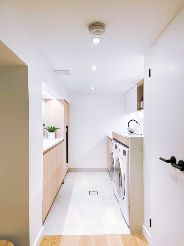 Photo of a large scandinavian galley utility room in Toronto with an utility sink, flat-panel cabinets, light wood cabinets, engineered stone countertops, multi-coloured splashback, porcelain splashback, white walls, ceramic flooring, a side by side washer and dryer, grey floors and grey worktops.