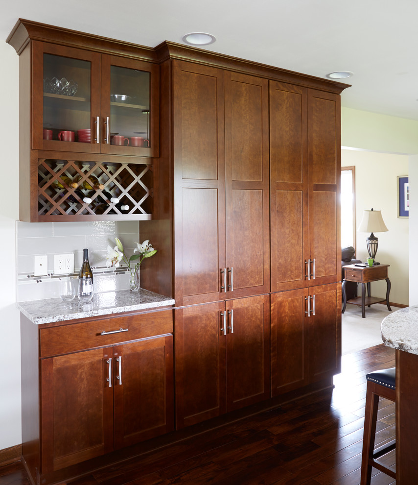 Large transitional l-shaped dark wood floor enclosed kitchen photo in Milwaukee with an undermount sink, shaker cabinets, medium tone wood cabinets, granite countertops, white backsplash, porcelain backsplash, stainless steel appliances and an island