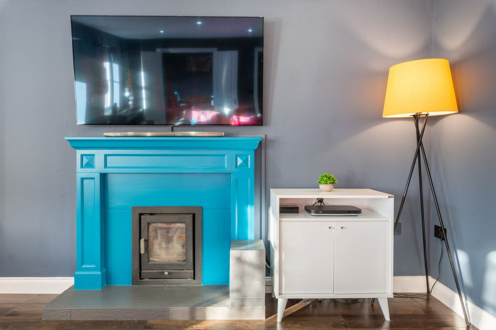 Mittelgroßes Modernes Wohnzimmer mit blauer Wandfarbe, Laminat, Kaminofen, verputzter Kaminumrandung, TV-Wand und braunem Boden in Kent