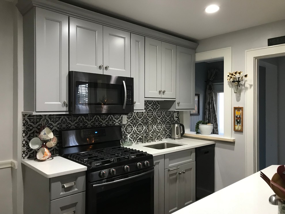 Small transitional galley medium tone wood floor and brown floor kitchen photo with an undermount sink, shaker cabinets, gray cabinets, quartz countertops, multicolored backsplash, porcelain backsplash, black appliances and no island