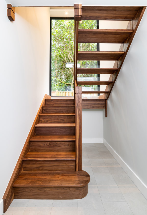 Large modern wood straight staircase in Kent with glass risers and glass railing.